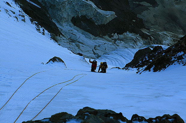 The roped team of two climbers climbs a steep slope before reaching the Ushba Ridge